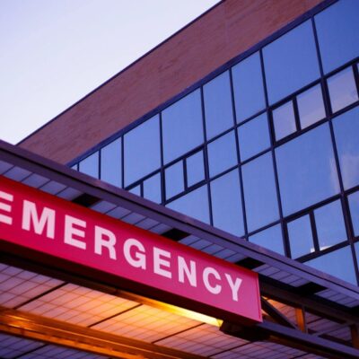 A hospital emergency sign is lit up at dusk.