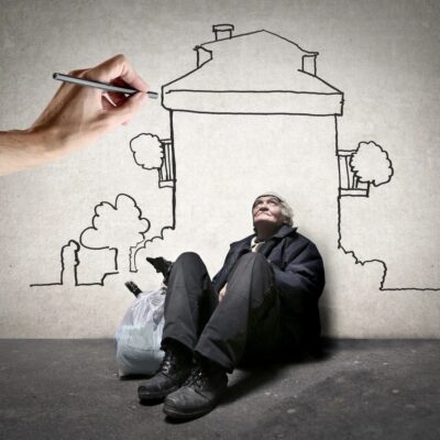 A homeless man sitting on the ground with a drawing of a house.