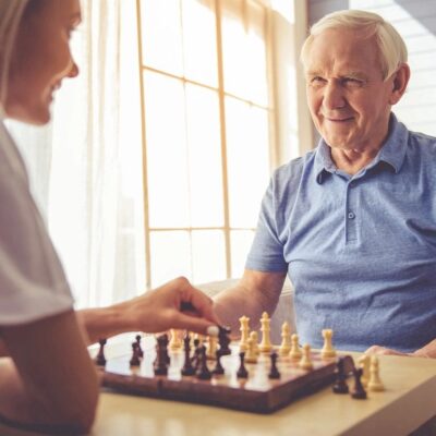 An elderly man and woman playing chess at home.