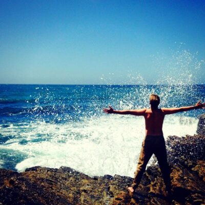A person standing on top of a rock near the ocean.