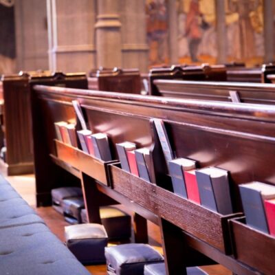 Wooden church pews with hymnals and cushions arranged neatly.