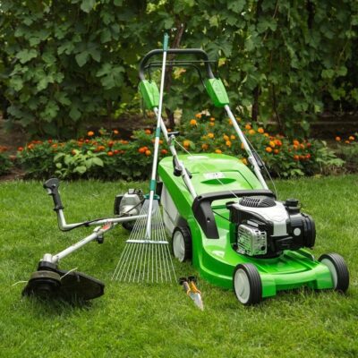 A green lawn mower and a rake in the grass.