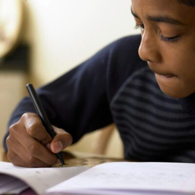 A boy writing in a notebook with a pen.