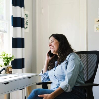 A woman talking on the phone while sitting in a chair in her home office.