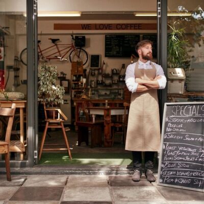 A man in an apron standing in front of a restaurant.