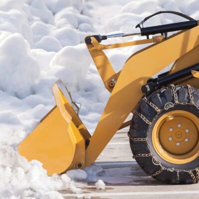 A yellow bulldozer is removing snow from a parking lot.