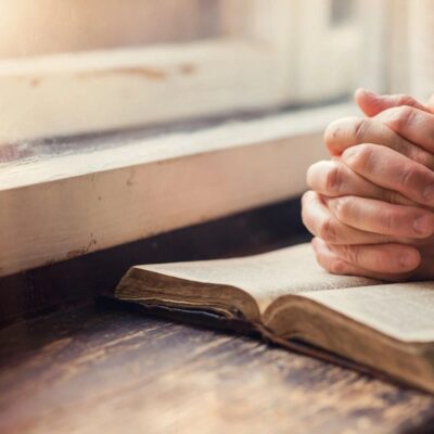 A woman praying with her hands on a bible.