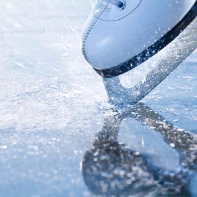 Close-up of an ice skate blade gliding on ice, creating ice shavings.