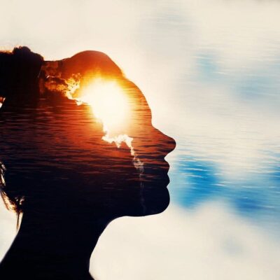 Silhouette of a woman with the sun shining through her head against a cloudy sky.