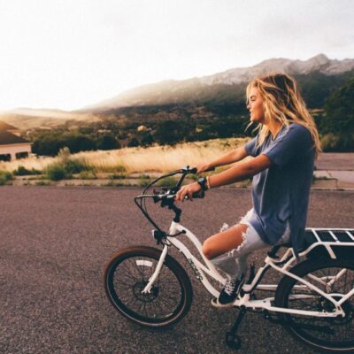 Young woman riding a bike on a road with mountains in the background.