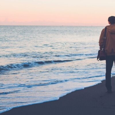 Man with bag on beach at sunset.