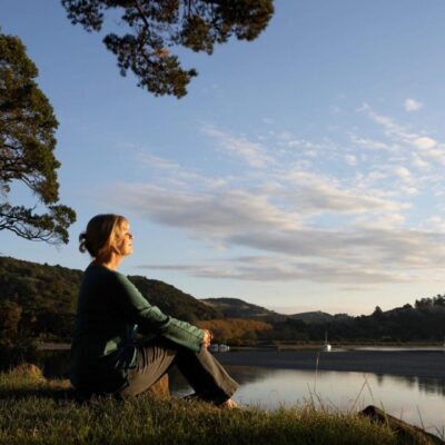 A woman sits on a rock overlooking a lake.