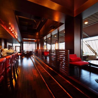 A bar with a wooden floor and red chairs.