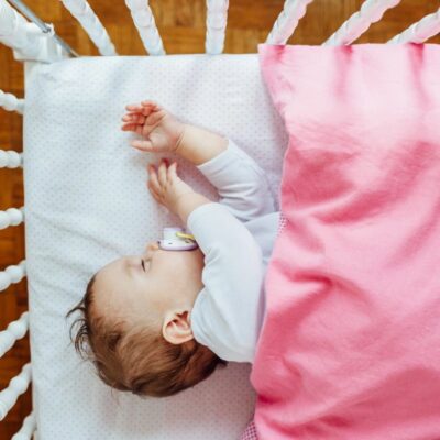 A baby sleeping in a crib with a pink blanket.