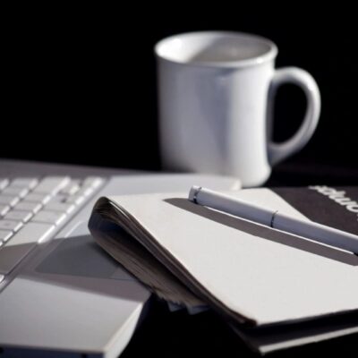 A notebook, a pen and a cup of coffee on a desk.