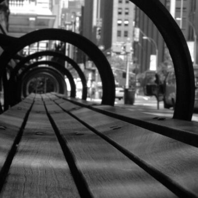 A black and white photo of a bench in a city.