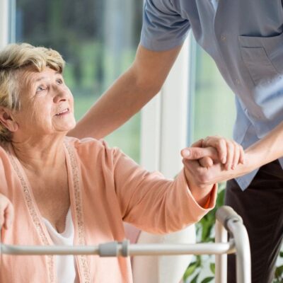 A nurse is helping an elderly woman on a walker.