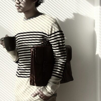 Man in striped sweater holding coffee and briefcase.