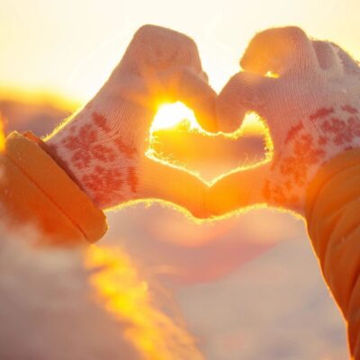 A woman is making a heart shape with her hands in the snow.