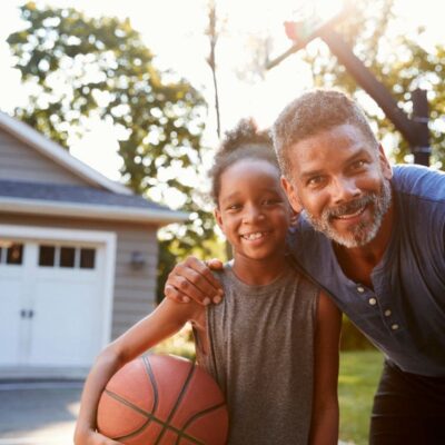 A man and a girl holding a basketball in front of a house.
