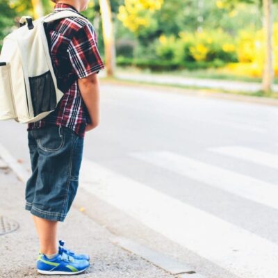 Child with backpack waiting at crosswalk.