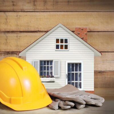 Construction helmet and gloves in front of a small house model.
