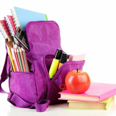 Purple backpack filled with school supplies and an apple on books.