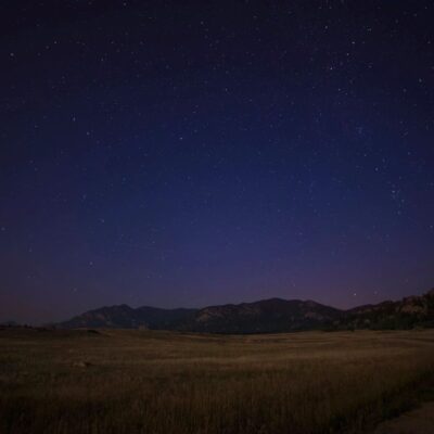 A starry sky over a grassy field and mountains.
