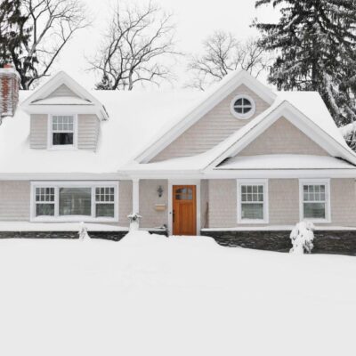 A snow-covered house with a wooden front door and surrounding trees.