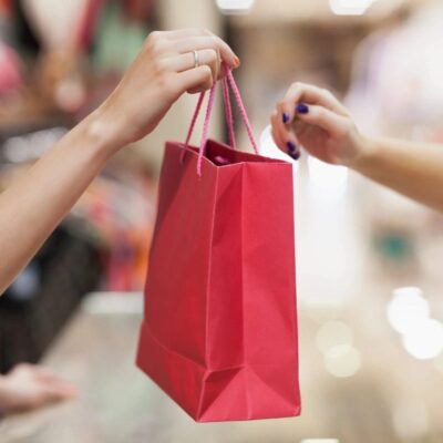 A woman handing a shopping bag to another woman in a store.