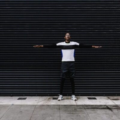 A man standing in front of a black wall with his arms outstretched.