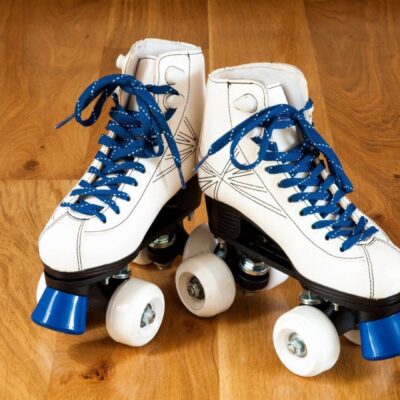 White roller skates with blue laces and wheels on a wooden floor.