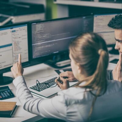Two people sitting at a desk with computers.