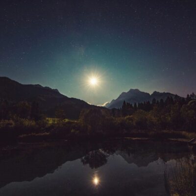 Night sky, moonlit mountains reflected in lake.