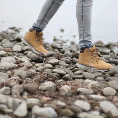 Person walking on rocky terrain wearing yellow boots and gray pants.
