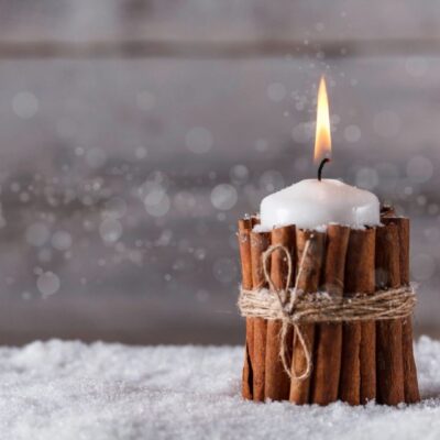 A candle with cinnamon sticks in the snow.