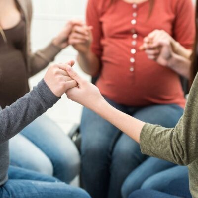 Pregnant woman with family holding hands in a supportive circle.