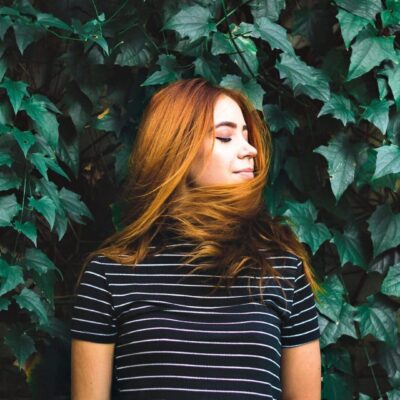 Redhead woman relaxing against green leaves.