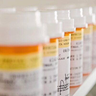 Many prescription bottles are lined up on a shelf.