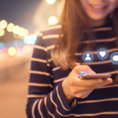 A woman holding a cell phone with social icons on it.