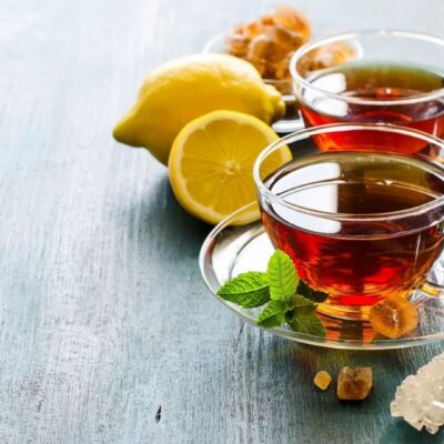 Two cups of tea with lemon and ginger on a table.