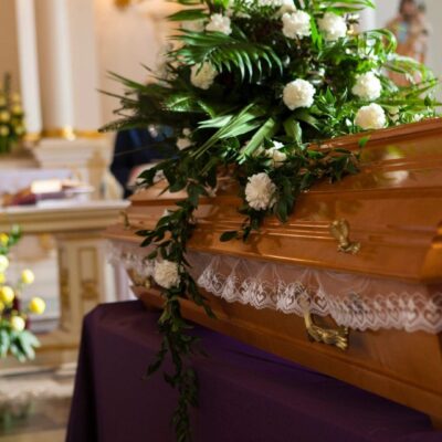 A flower-adorned wooden coffin in a solemn funeral setting.