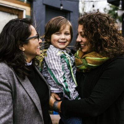Two women holding a child in front of a house.