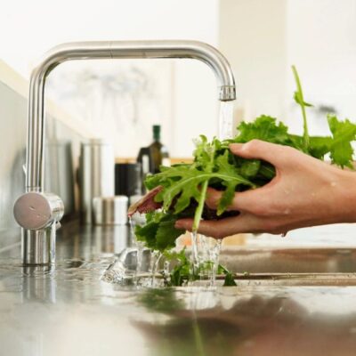 A person is washing greens in a kitchen sink.