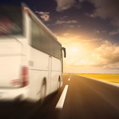 A white bus is driving down the road at sunset.