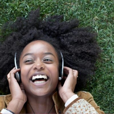 A young woman with afro hair listening to music in the grass.