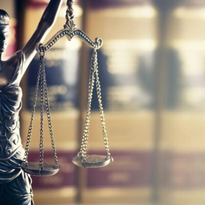 A statue of justice holding scales in front of books.