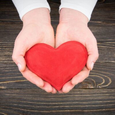 A woman's hands holding a red heart on a wooden table.
