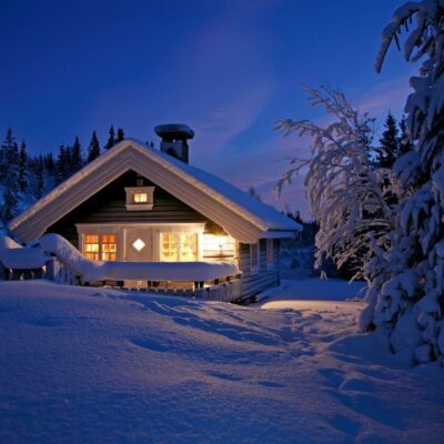 Cozy cabin warmly lit in snowy winter evening.