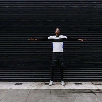 A man standing in front of a black wall with his arms outstretched.